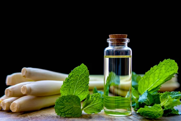 Naneli ve limonotlu esasen naneli ve limonlu yağ şişesi, ahşap bir tabağa konmuş ve siyah bir arka planı var..