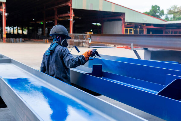 The painter is working to painting color top coat on steel structure with spray gun, at industrial factory.