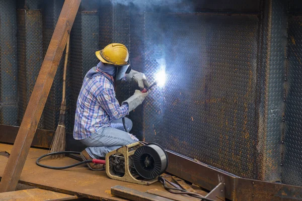 The welder is welding a steel structure work with process Flux Cored Arc Welding(FCAW) and dressed properly with personal protective equipment(PPE) for safety, at industrial factory.