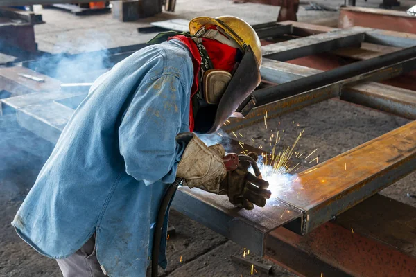 The welder is welding a steel structure work with process Flux Cored Arc Welding(FCAW) and dressed properly with personal protective equipment(PPE) for safety, at industrial factory.