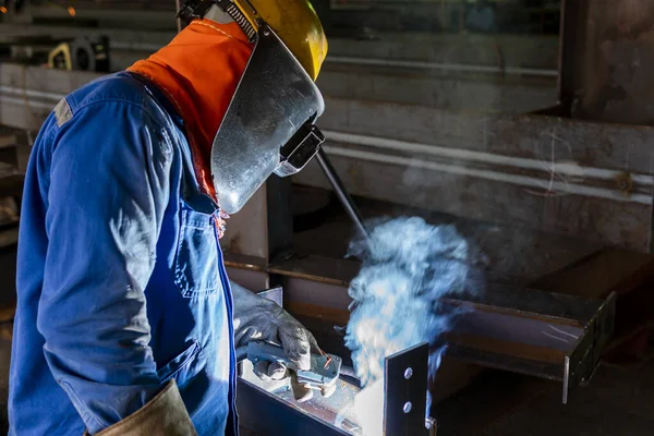 The welder is welding a steel structure work with process Flux Cored Arc Welding(FCAW) and dressed properly with personal protective equipment(PPE) for safety, at industrial factory.