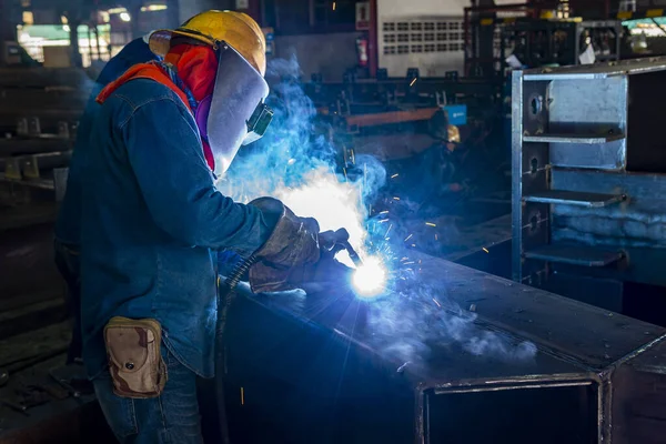 The welder is welding a steel structure work with process Flux Cored Arc Welding(FCAW) and dressed properly with personal protective equipment(PPE) for safety, at industrial factory.