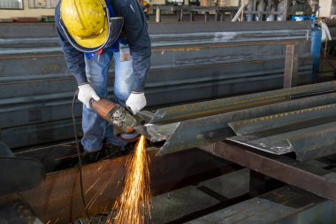 İşçi, endüstriyel fabrikada kestikten sonra H-ışını çeliğinin yüzeyini öğütmek için öğütme makinesi kullanılıyor..