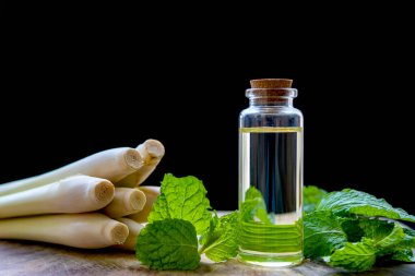 Naneli ve limonotlu esasen naneli ve limonlu yağ şişesi, ahşap bir tabağa konmuş ve siyah bir arka planı var..