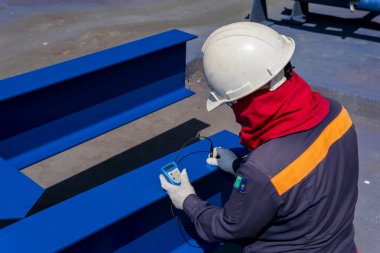 Teknisyenler, endüstriyel fabrikadaki çelik yapının boyanması için Kalın Kaplama Ölçeği (DFT) ile Kuru Film Kalınlığını ölçüyorlar..