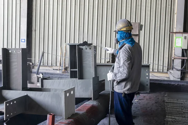 The painter is working to painting the steel structure with spray gun at industrial factory.