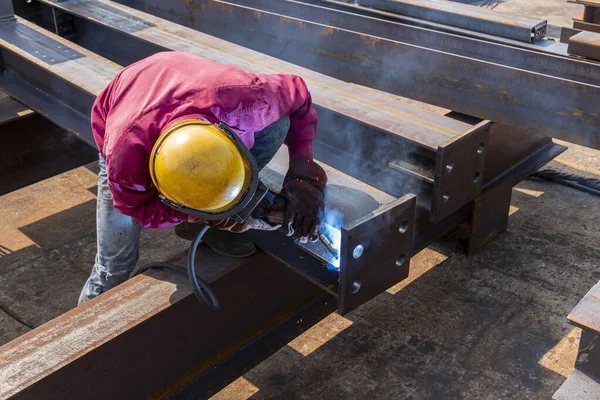 The welder is welding a steel structure work with process Flux Cored Arc Welding(FCAW) and dressed properly with personal protective equipment(PPE) for safety, at industrial factory.