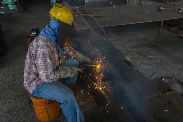 The welder is welding a steel structure work with process Flux Cored Arc Welding(FCAW) and dressed properly with personal protective equipment(PPE) for safety, at industrial factory.