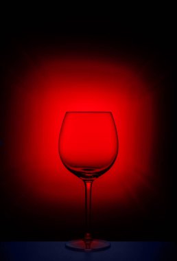Koyu arkaplanda kırmızı ışıkta yansıması olan boş şarap kadehi