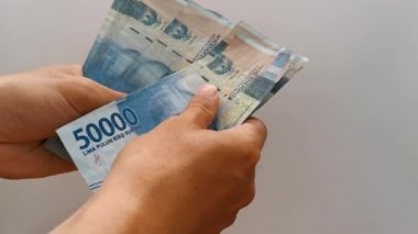 Endonezya parası sayılıyor. Beyaz gri arka planda elli bin rupia.