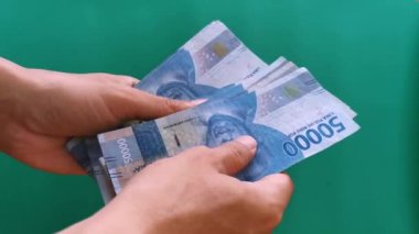 Endonezya parası sayılıyor. Yeşil arka planda elli bin rupia.