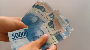 Endonezya parası sayılıyor. Beyaz gri arka planda elli bin rupia.