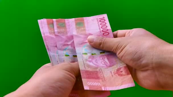 Contando dinero Rupia indonesia Rp. 100000 (Cien mil rupias) a mano en efectivo sobre fondo verde. Mostrando 10 billetes en la cantidad de 1000000 rupias — Vídeo de stock
