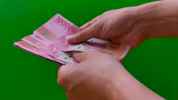 Contando dinero Rupia indonesia Rp. 100000 (Cien mil rupias) a mano en efectivo sobre fondo verde. Mostrando 10 billetes en la cantidad de 1000000 rupias — Vídeos de Stock