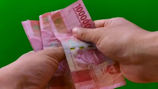 นับเงินรูเปียห์อินโดนีเซีย 100,000 (หนึ่งแสนรูปี) ด้วยเงินสดบนพื้นหลังสีเขียว แสดงธนบัตร 10 ใบในปริมาณ 10,00000 รูปี — วีดีโอสต็อก