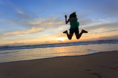 kadın Gezgin gündoğumu ile sahilde atlama mutlu