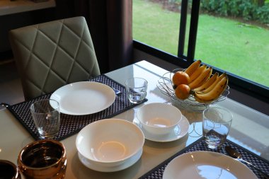 Çanak çömlek setleri yemek masasında modern ev içi yemek odasının içinde pencerenin dışında yeşil bahçeli.