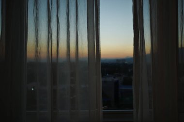 pencerenin dışında gün batımı gökyüzü görünümü ile beyaz perde ile güneş ışığı