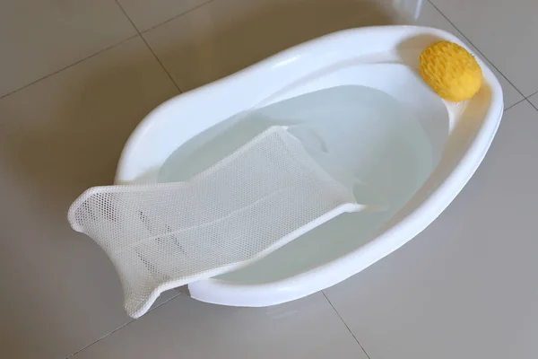 Babybadkar med stödsäte för nyfödda som sitter i vatten och mjuk svamp — Stockfoto