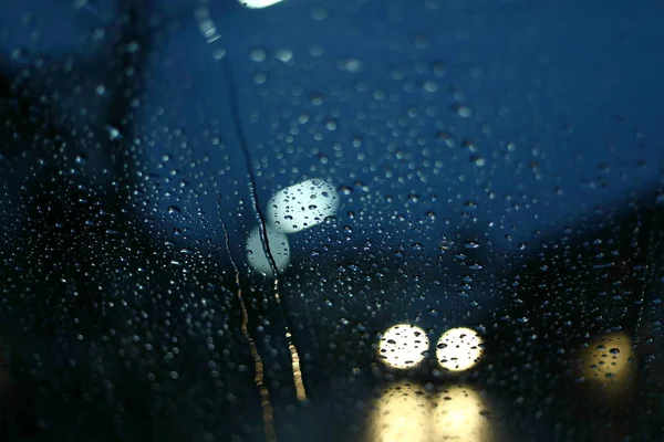 Βροχή νερού πτώση σε γυάλινο παράθυρο με θαμπάδα φως του δρόμου στο φόντο της πόλης νύχτα — Φωτογραφία Αρχείου