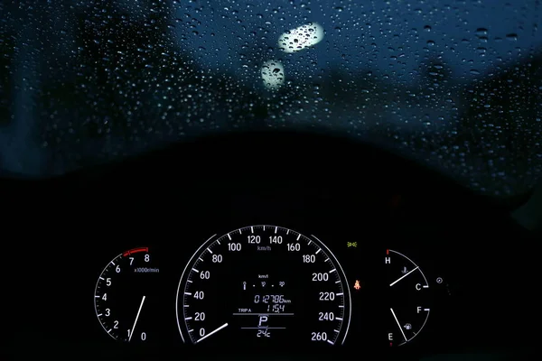 Hastighetsmätare nattljus i modern bil med regn droppe på fönstret — Stockfoto