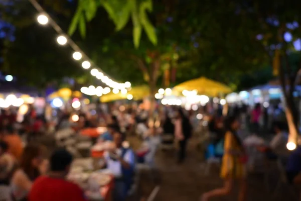 people crowd in night party festival of outdoor garden with light bulb hanging decoration