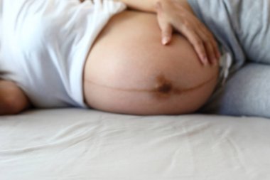 Anne yatakta dinleniyor, kadın el ele tutuşuyor hamile karnını sevgiyle kucaklıyor.