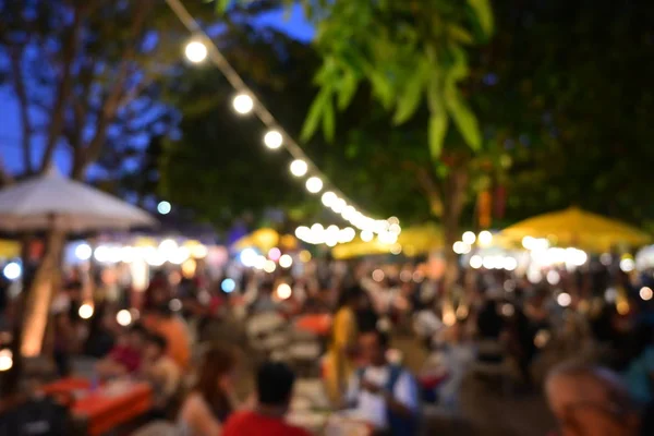 people crowd in night party festival of outdoor garden with light bulb hanging decoration