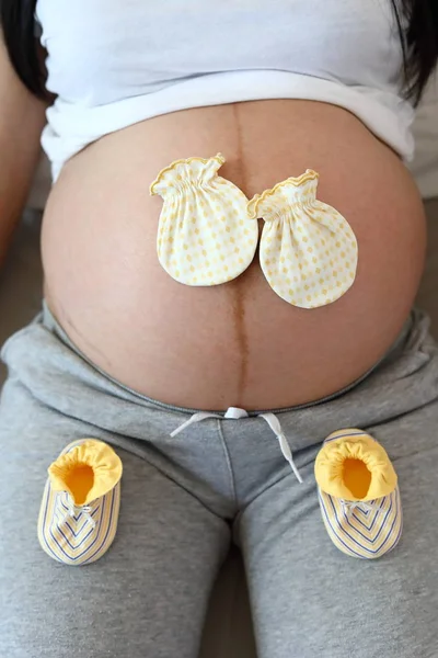 Söt liten handske och strumpa sätta på mamma magen gravid väntar på baby nyfödda — Stockfoto