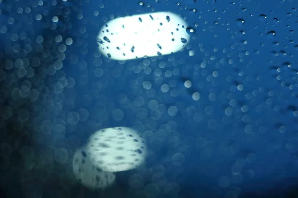 Gota de lluvia de agua en la ventana de cristal con luz de calle borrosa en el fondo de la ciudad noche — Foto de Stock