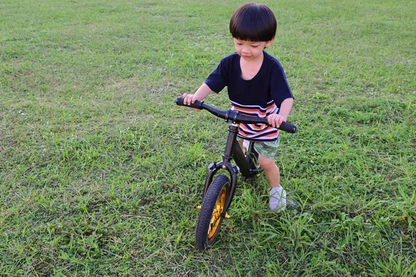 Cute boy playing balance bike on grass field of playground — 스톡 사진