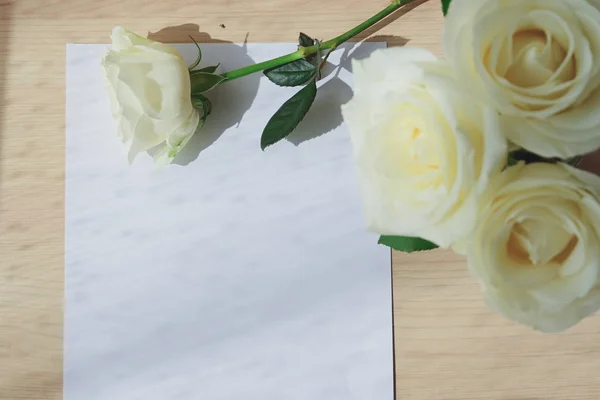 Carta vacía de papel en blanco y rosa blanca sobre mesa de madera con luz de ventana en el día de la mañana —  Fotos de Stock