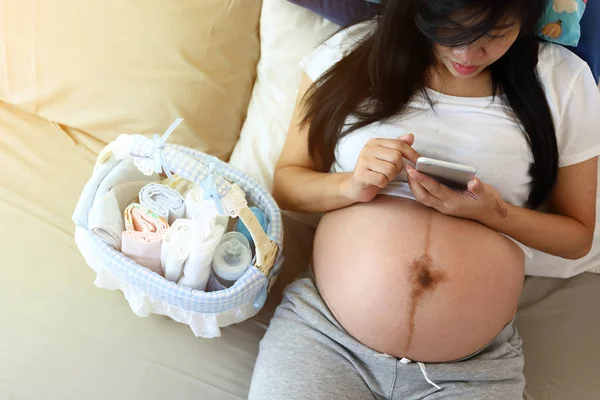 Moeder zwanger zitten ontspannen op het bed met luier en fles en melk in baby mand — Stockfoto