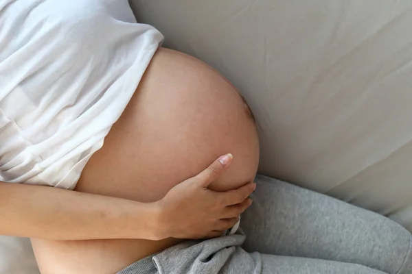 Matka odpočívající na posteli, žena ruka objímající těhotné bříško s láskou — Stock fotografie