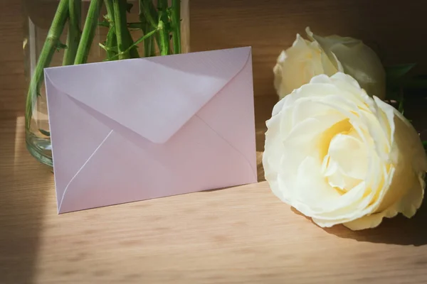 Pink envelope letter and white rose flower on wood table with sunlight in the morning — Stock Photo, Image