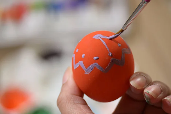 Personas que utilizan pintura pincel acuarela púrpura en naranja Pascua huevo diseño patrón personalizado artesanía para la celebración — Foto de Stock