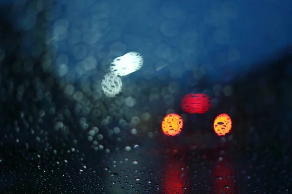 Gota de chuva de água na janela de vidro com luz de rua desfocada no fundo da cidade noite — Fotografia de Stock
