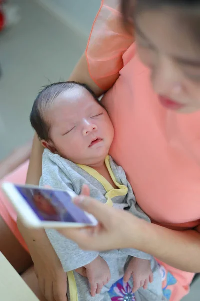 Ibu bermain ponsel di kantor bisnis rumah tangga dengan bayi lucu yang baru lahir tidur — Stok Foto