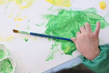 Bebek, beyaz kağıt arka planda boyasız el fırçası kullanarak yeşil ve sarı sulu boya kullanıyor.