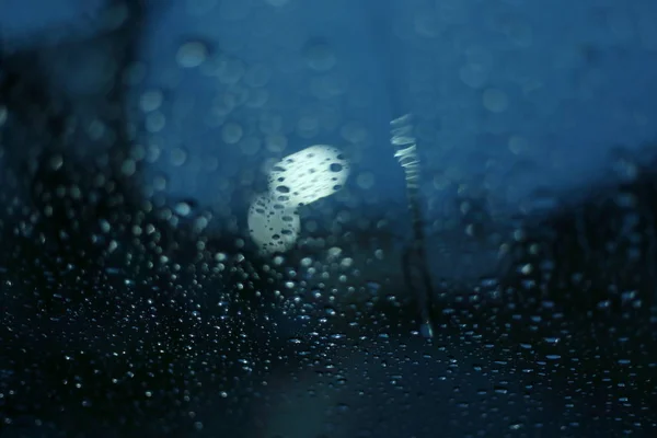 Капли дождя на стеклянное окно с размытой улице света в ночном фоне города — стоковое фото