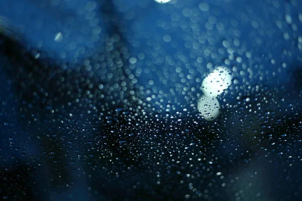 Gota de lluvia de agua en la ventana de cristal con luz de calle borrosa en el fondo de la ciudad noche — Foto de Stock