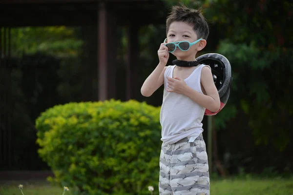 Heureux garçon mignon porter des lunettes de soleil et un casque de sport en jouant à vélo exercice dans le parc — Photo