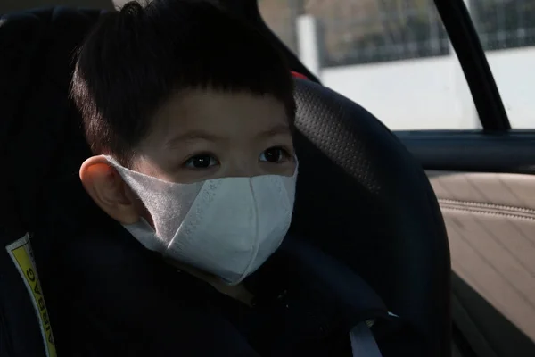 Дитина сидить на автокріслі в гігієнічній масці для захисту обличчя догляд за собою від хвороб, що поширюють інфекцію та забруднення повітря — стокове фото