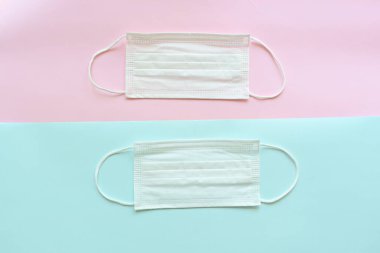 Pembe ve mavi pastel arka planda tıbbi yüz maskesi.