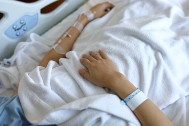 Kadın hasta yatağında dinleniyor, elinde serum, serum, damar içi enjeksiyon ilaçları var. Hastanedeki hastalıkları iyileştirmek için.