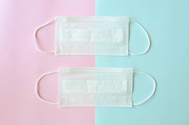 Pembe ve mavi pastel arka planda tıbbi yüz maskesi.