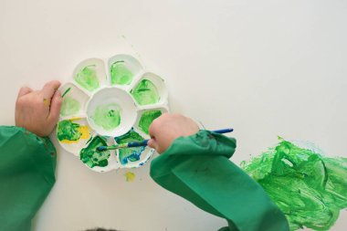 Bebek, boyasız el fırçası kullanıyor. Beyaz kağıt arka plan üzerinde yeşil ve sarı suluboya boya. Renkli ve soyut bir hayal gücü var.