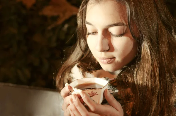 Chica sentada en el banch en un parque de noche y tomando una taza de té. — Foto de Stock