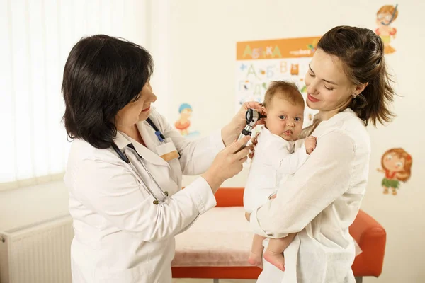Doktor bir kulak denetlendiği sırada bir bebek tutan anne