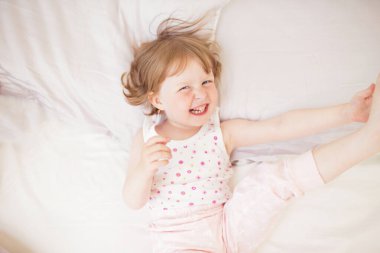 Pijamayla yatakta gülen küçük kız.
